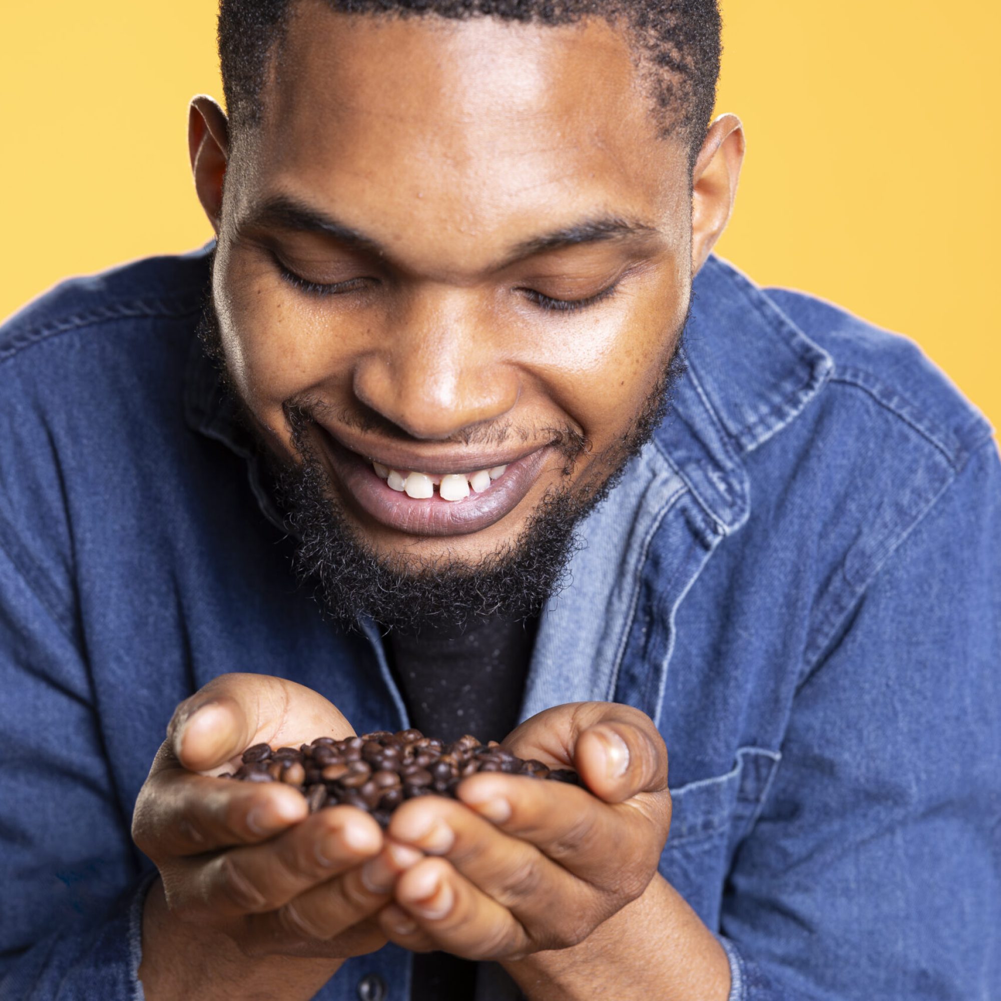 Coffee lover savoring the fresh aromatic black roasted scent, enthusiastic man holding a handful of coffee beans up to his nose and enjoying the c0old brew aroma, delicious flavor.